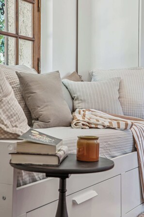 Una habitación acogedora con una cama, almohadas, una mesa con un libro y una vela, y una ventana con vistas.