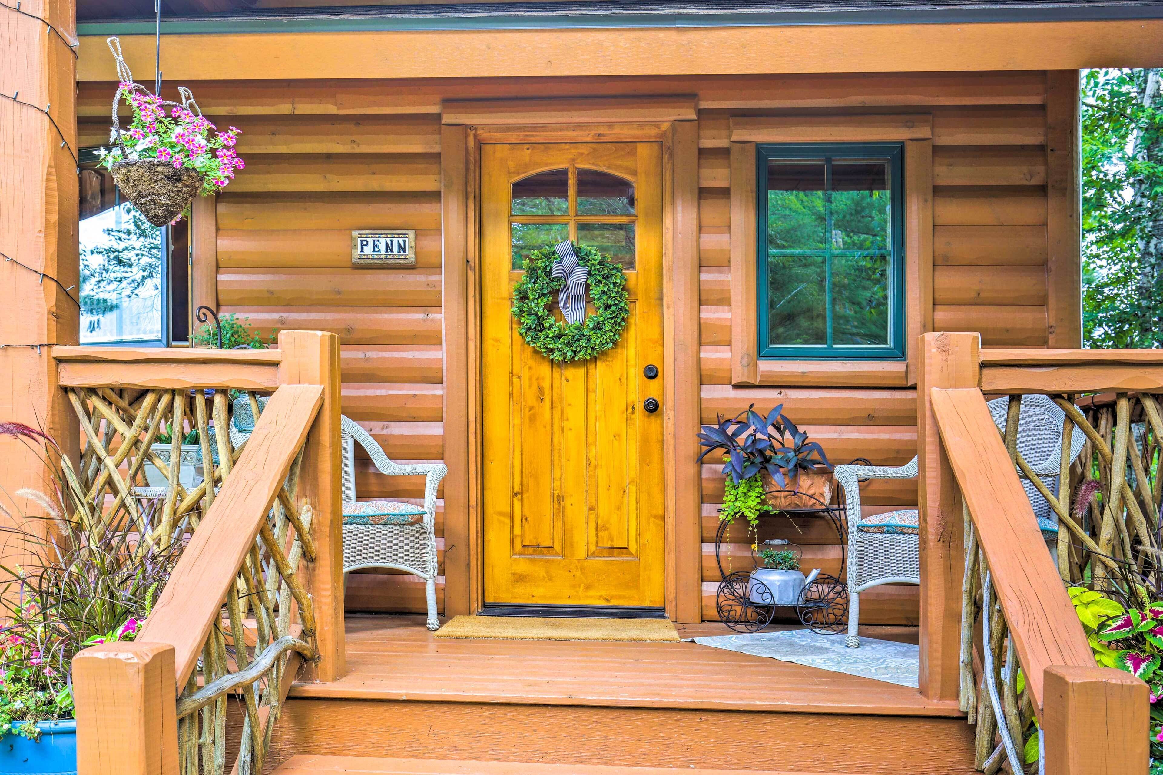 Una cabaña de madera con una puerta amarilla, un adorno de bienvenida y sillas de mimbre en el exterior.