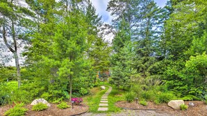 Un sentier de jardin qui traverse une zone bois ée, avec un chemin pavé de pierres, bordé de différentes plantes et arbres.