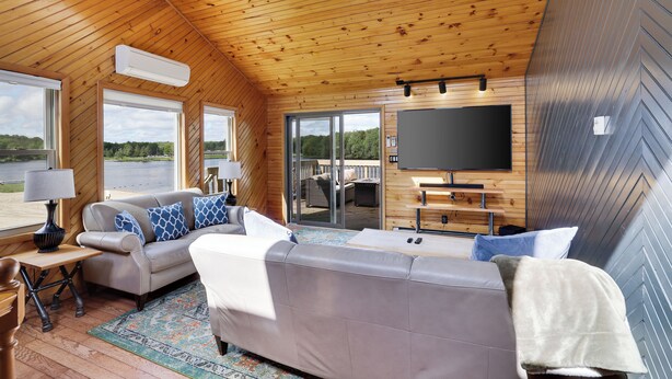 Indretning i en hyggelig hytte med træloft, stort fjernsyn og sofa med mønstrede puder.