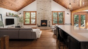 Un amplio espacio habitable con chimenea de piedra, techo de madera y ventanas grandes.