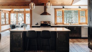 Una cocina moderna con una isla grande, techo de madera y amplios ventanales con vistas a árboles.