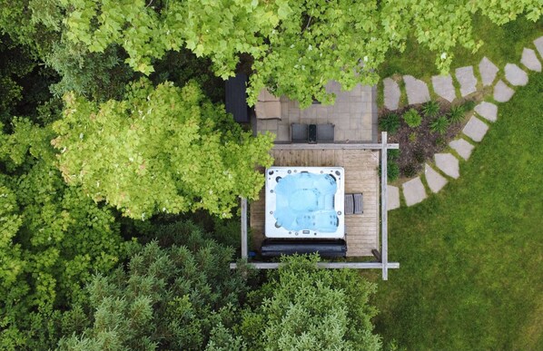 Vista aérea de un jacuzzi sobre una terraza de madera rodeada de exuberante vegetación.