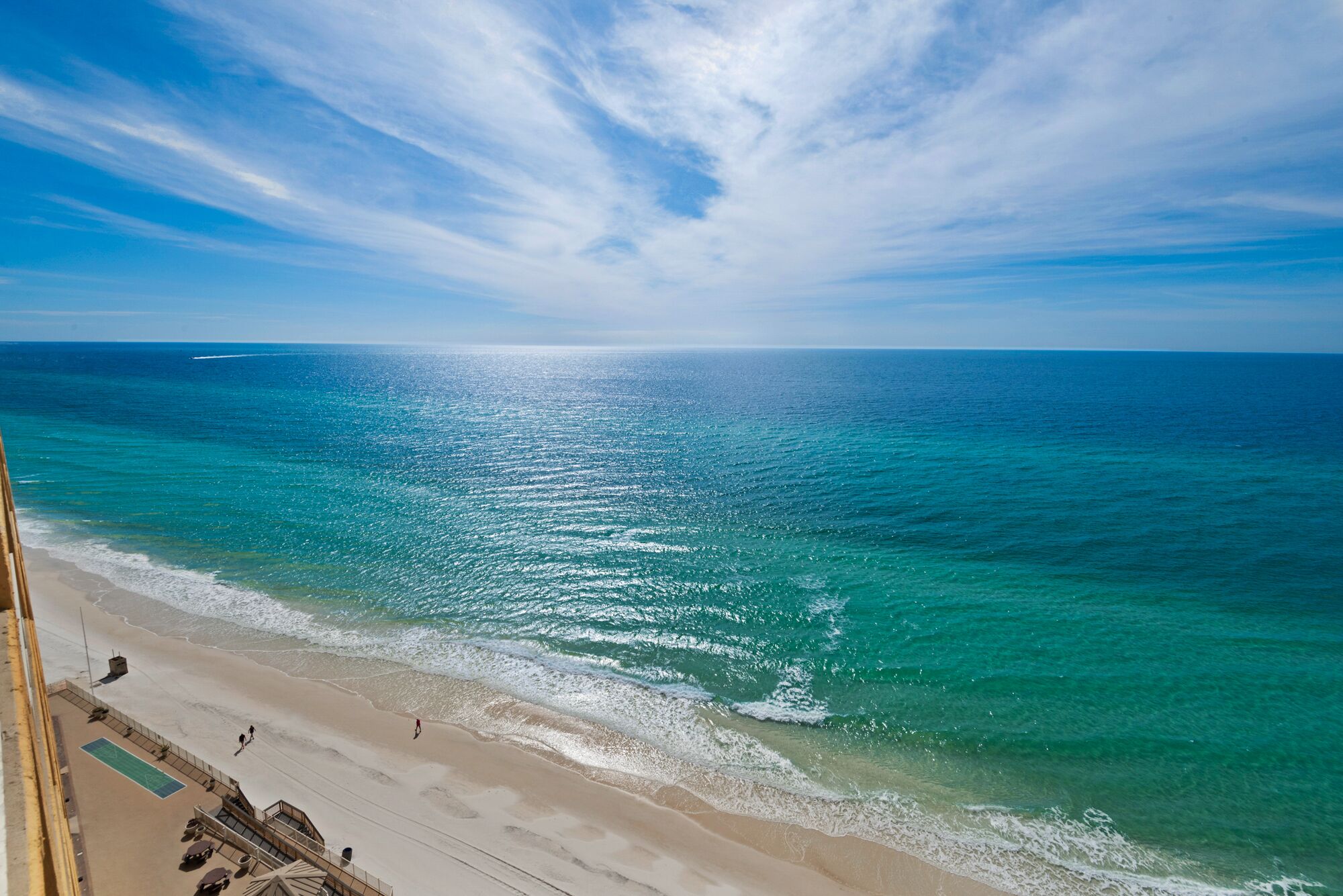 Blick auf einen Strand mit blauem Himmel, ruhiger See und sandigem Ufer.