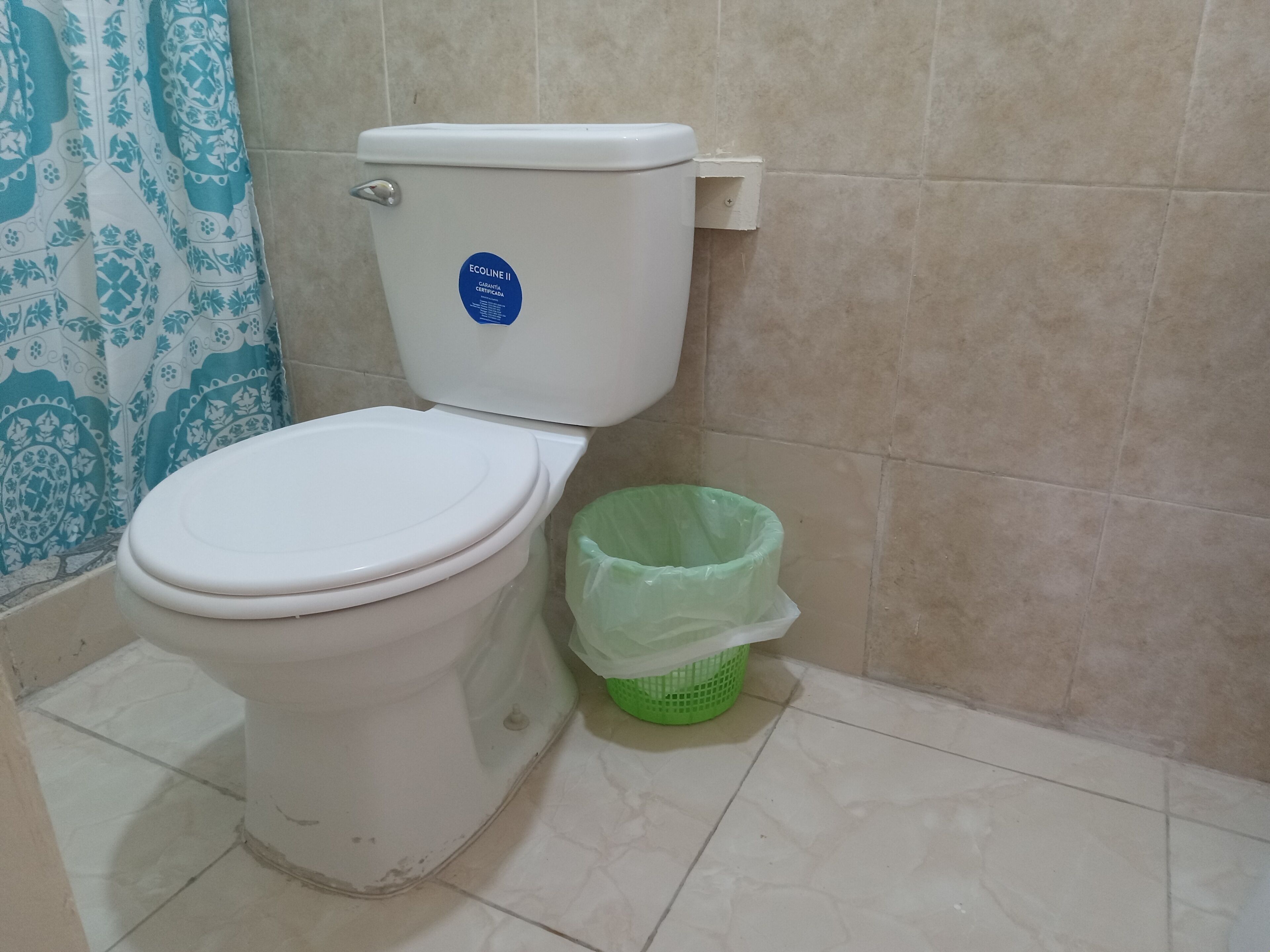 Des toilettes ornées d’un autocollant bleu, une poubelle verte et un rideau à motifs dans une salle de bain.
