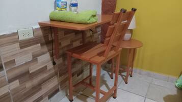 Una habitación pequeña con una mesa y silla de madera, una toalla verde, una botella de agua y una caja de pañuelos.