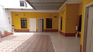 A covered outdoor area with tiled flooring, yellow walls, and multiple doors. - Hotel Piedras Bonitas (Siguatepeque)