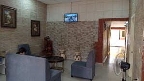 A lobby with a brick wall, a television mounted on the wall, two sofas, a small round table, and a standing fan. - Hotel Piedras Bonitas (Siguatepeque)
