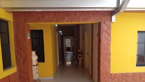 A hallway with yellow walls and a tiled floor, leading to a room with a window and a door. - Hotel Piedras Bonitas (Siguatepeque)
