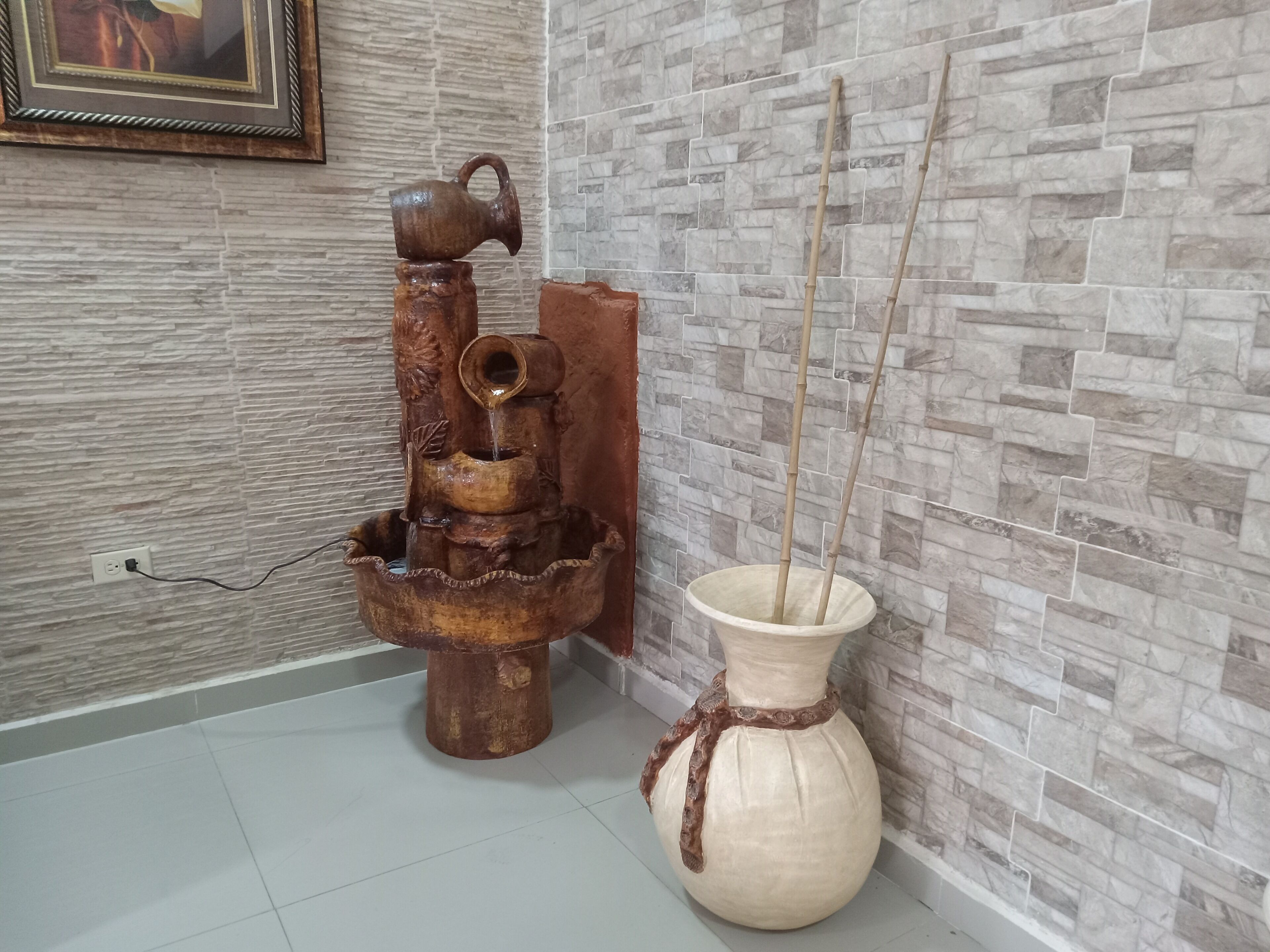Una fuente rústica con base de madera y un florero con ramas de bambú.