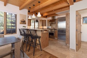 A spacious kitchen with wooden beams, a central island with bar stools, and a large refrigerator.