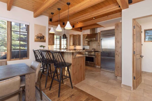 A spacious kitchen with wooden beams, a central island with bar stools, and a large refrigerator.