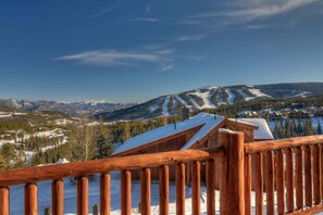 A wooden deck overlooking a snowy mountain landscape with a ski resort in the background. - Ski-In/Ski-Out Big Sky Home with Incredible Views (Big Sky)