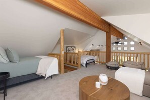 Une chambre mansardée chaleureuse, avec un lit en mezzanine, un canapé, une table basse en bois et une vue sur l’extérieur par une fenêtre.