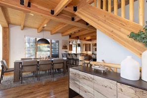 A spacious kitchen with wooden beams, a dining area with a large table and chairs, and a view of the outdoors through a window.