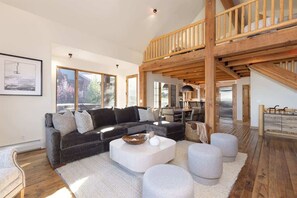 A modern living room with a dark grey sofa, white ottomans, and a wooden staircase.
