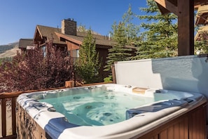 A hot tub on a wooden deck with a view of a mountain and a wooden house in the background.