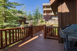 A wooden deck with a railing, leading to a building with a stone facade and a balcony.