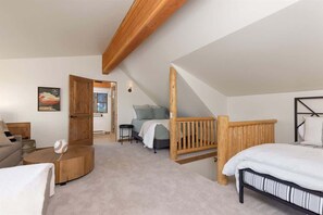 A bedroom with a loft bed, a wooden headboard, a small seating area, and a door leading to another room.