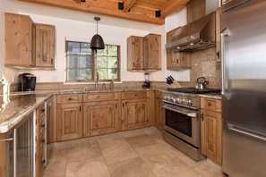 A kitchen with wooden cabinets, a stainless steel refrigerator, a stove, and a window with a view of greenery.