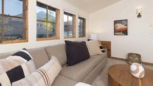A living room with a sofa, a round wooden coffee table, and a lamp. - Ski-In/Ski-Out Big Sky Home with Incredible Views (Big Sky)