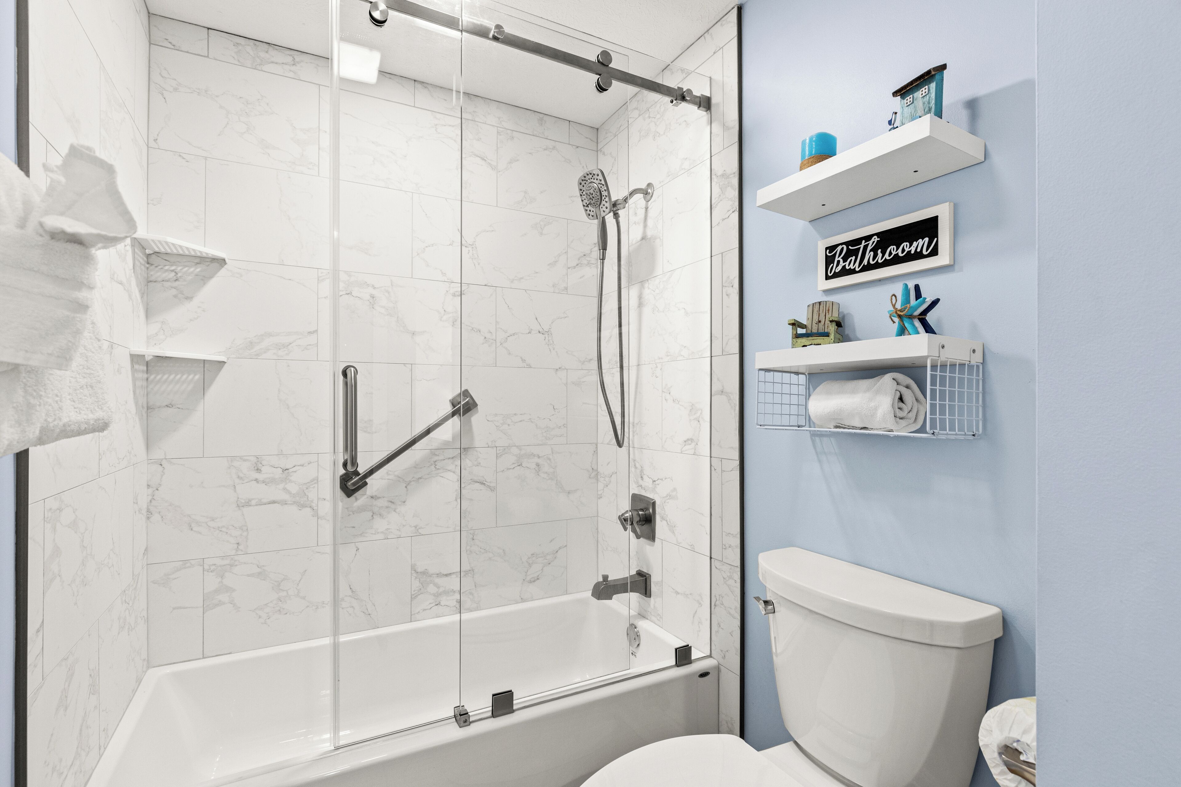 A modern bathroom with a glass-enclosed shower, a white toilet, and a "Bathroom" sign on the wall.