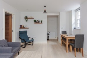 Ein modernes Wohnzimmer mit einem blauen Sessel, einem grauen Sofa, einem Holzesstisch mit zwei Stühlen und einem weißen Heizkörper.