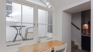 A dining area with a wooden table and chairs, a window with a view of the outside, and a staircase leading to an upper level.