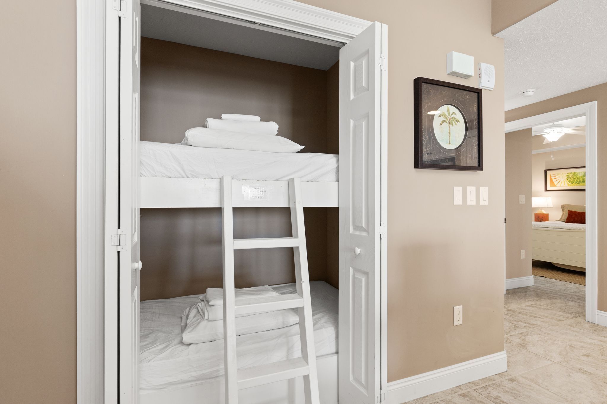 Una habitación con literas, una escalera, un cuadro en la pared y una puerta que da a otra habitación.
