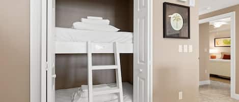 Una habitación con literas, una escalera, un cuadro en la pared y una puerta que da a otra habitación.