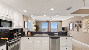 A modern kitchen with white cabinets, stainless steel appliances, and a large island. - Treasure Island 1806 (Panama City Beach)