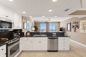 A modern kitchen with white cabinets, stainless steel appliances, a dishwasher, and a large window with a view. - Treasure Island 1806 (Panama City Beach)