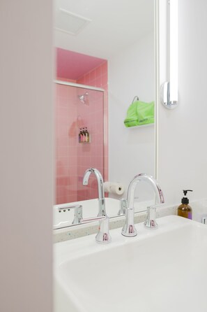 A bathroom with a white sink, two faucets, a mirror, and a shower with pink tiles. - The Gallatin (211) East Nashville Boutique Hotel (Nashville)