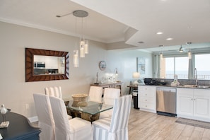 A modern kitchen with white cabinets, a dining area with striped chairs, and pendant lighting. - Treasure Island 1811 (Panama City Beach)