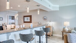 Une cuisine moderne dotée d’un îlot central, de tabourets de bar, de luminaires suspendus et d’une horloge murale.