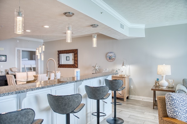 Una cocina moderna con una isla central, taburetes de bar, luces colgantes y un reloj en la pared.