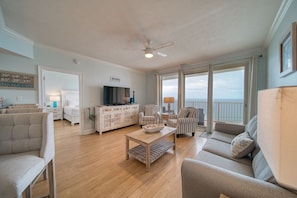 Relax in this spacious living room with a high ceiling and ocean views, featuring a sofa, chair, coffee table, and mounted TV.