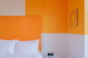 A hotel room with an orange and white color scheme, a bed with white linens, a digital clock, and a framed picture on the wall. - The Gallatin (Standard Queen) Gives back to community! (Nashville)