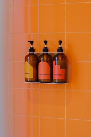 Three bottles of shampoo, conditioner, and body wash on a shelf against an orange tiled wall.