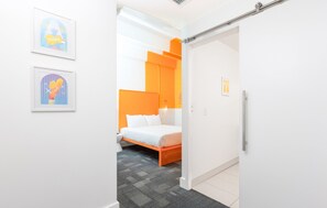 A modern hotel room with a bed, a nightstand, a wardrobe, and two framed artworks on the wall. - The Gallatin (Standard Queen) Gives back to community! (Nashville)