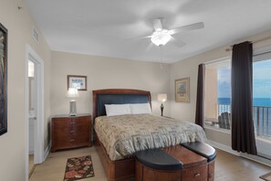 Ein Schlafzimmer mit Bett, Nachttischen, Deckenventilator, Fenster mit Vorhängen und Meerblick.