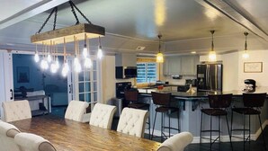 Une cuisine moderne dotée d’un îlot central, d’appareils électroménagers en acier inoxydable et de luminaires suspendus.