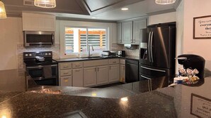 Une cuisine moderne dotée de plans de travail en granit, d’appareils électroménagers en acier inoxydable et de luminaires suspendus.