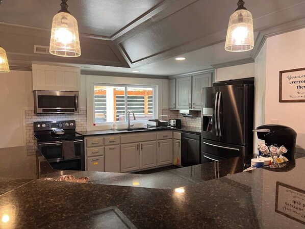 A modern kitchen with granite countertops, stainless steel appliances, and pendant lighting.
