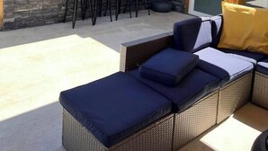 Une terrasse extérieure avec un canapé en osier, un mur en pierre et un coin bar équipé de tabourets.