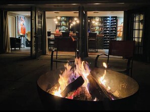 A bar area with a fire pit, seating, and a bar stocked with bottles.