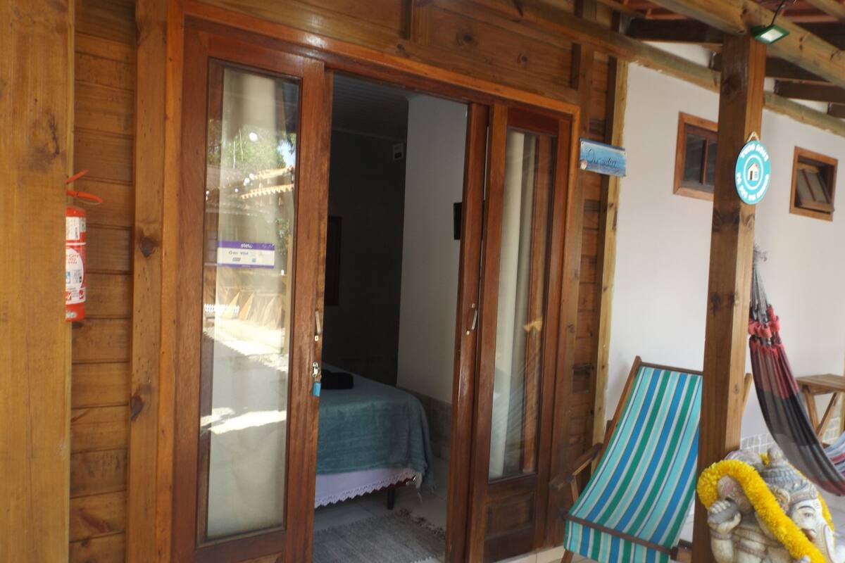 Quarto de madeira com cama, rede e uma estátua.