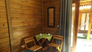 Um quarto de madeira com uma cama, uma mesa com toalha verde e uma cadeira.