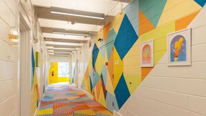 A brightly colored hallway with geometric patterns on the walls and floor, lockers, and framed artwork. - The Gallatin(214) Colorful Boutique Hotel (Nashville)
