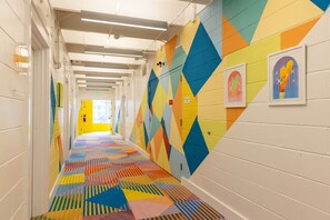 A brightly colored hallway with geometric patterns on the walls and floor, lockers, and framed artwork. - The Gallatin(214) Colorful Boutique Hotel (Nashville)